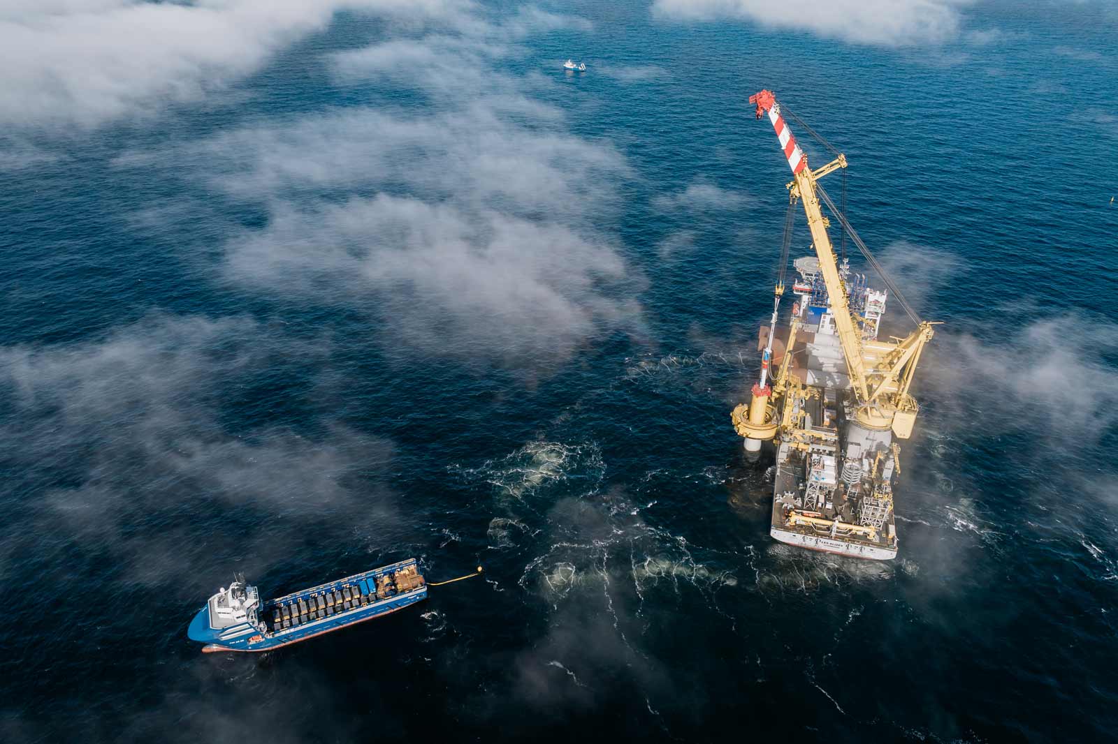 An oil vessel operates near an offshore platform surrounded by light fog and blue sea water.