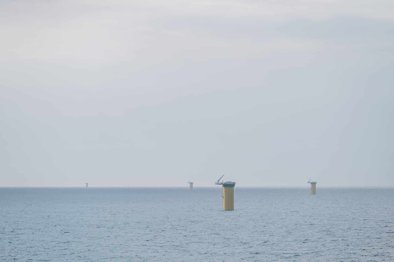 Four yellow platforms stand in the sea under a grey sky. They appear to be part of a wind farm.