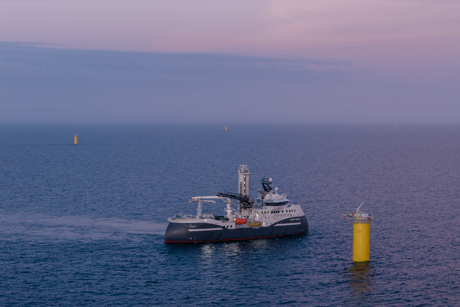A ship sails near a yellow pillar in the sea, with a luminous sky in the background.