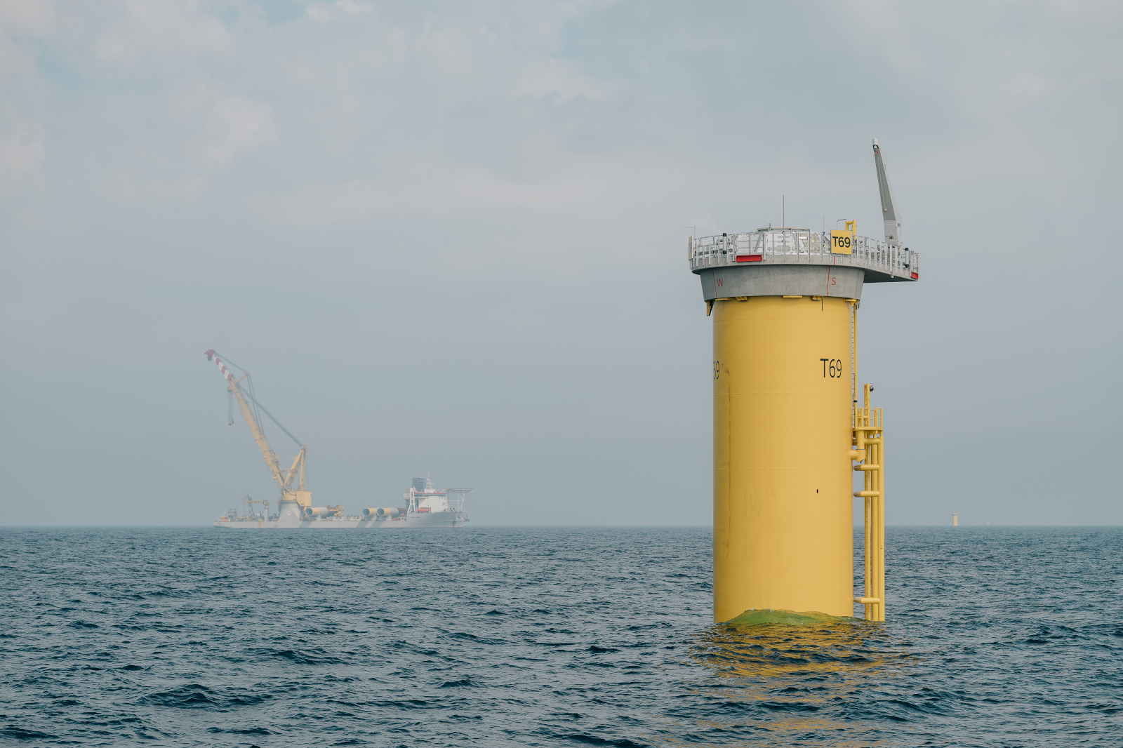 A yellow offshore wind platform is in the water, with a crane visible in the background.