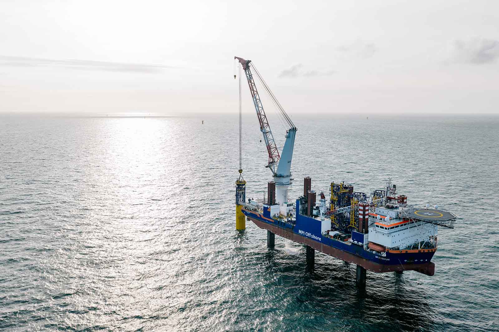 An offshore vessel with a crane lifting a cylinder over the sea under a cloudy sky.