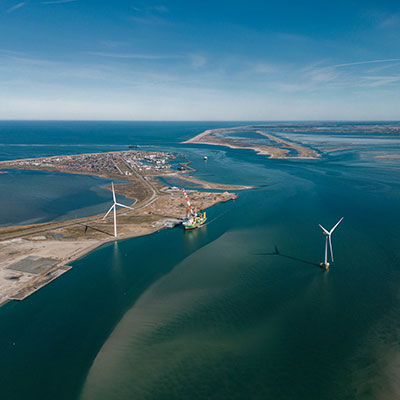 Et luftbillede af en kystlinje med vindmøller, en båd og en klar blå himmel.
