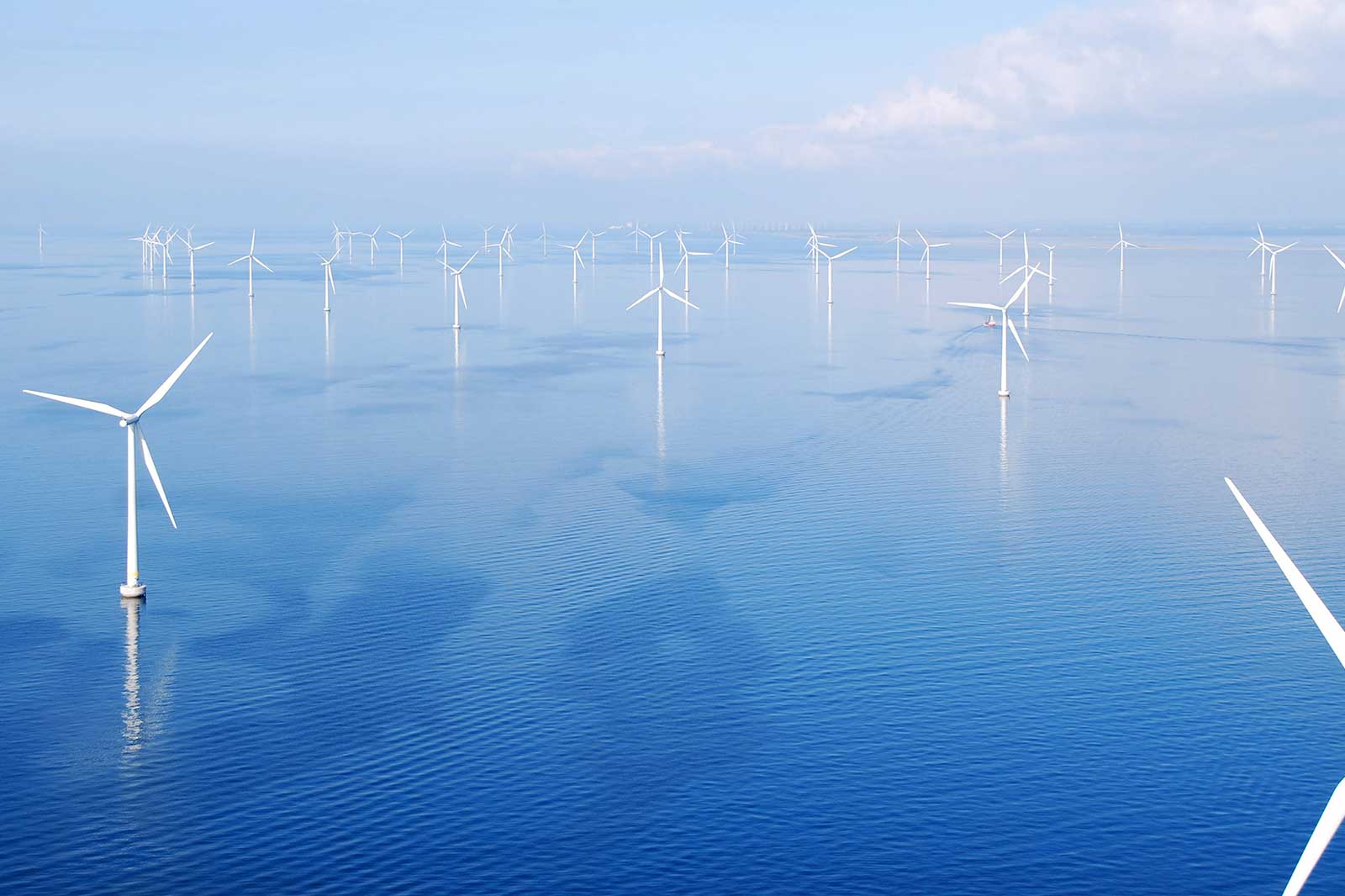 A panoramic view of a wind farm in the sea, featuring numerous wind turbines reflected on the calm blue water.