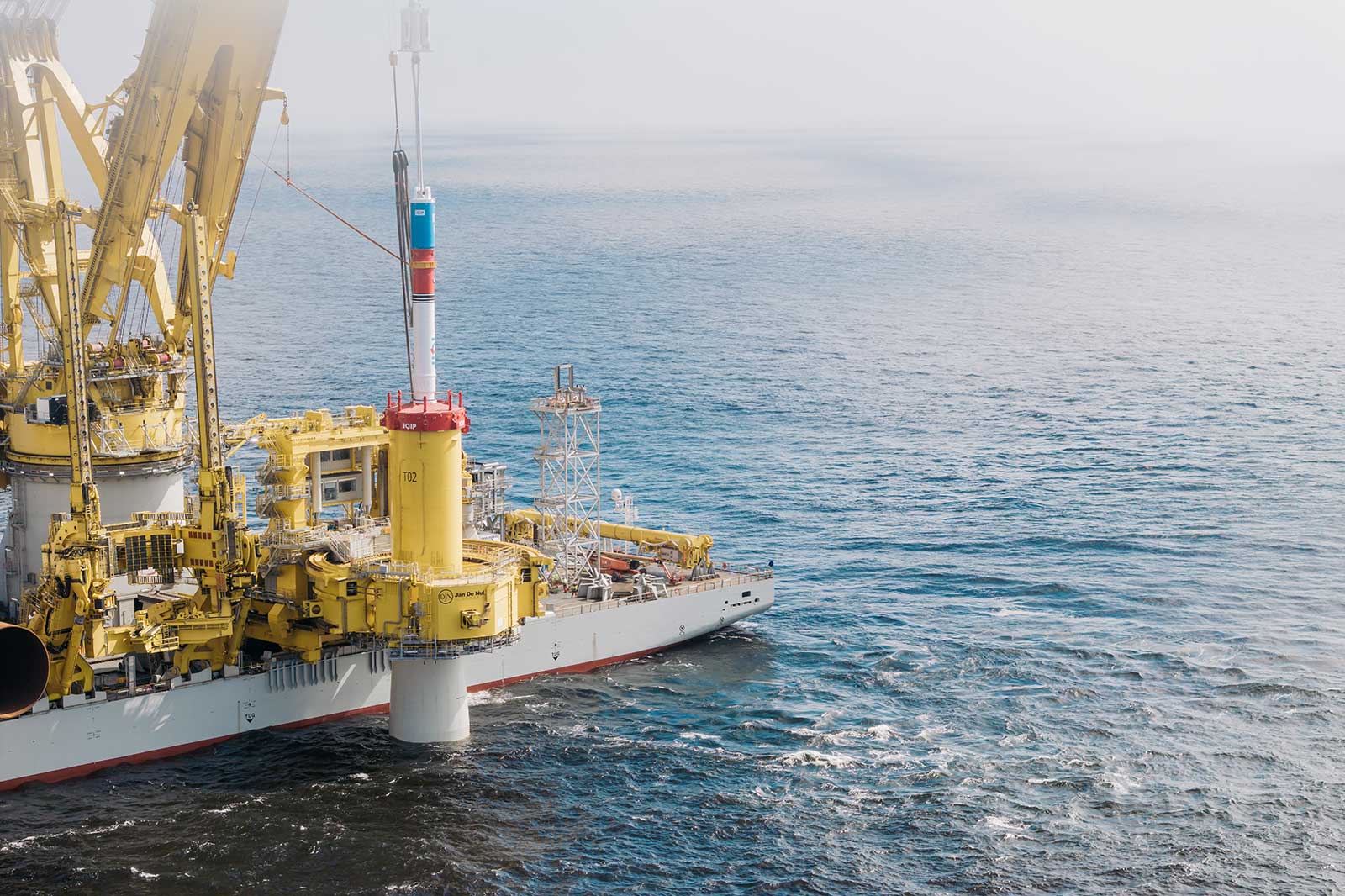 An offshore oil platform in yellow and white sits on the ocean surface with clear waves and a sky in the background.
